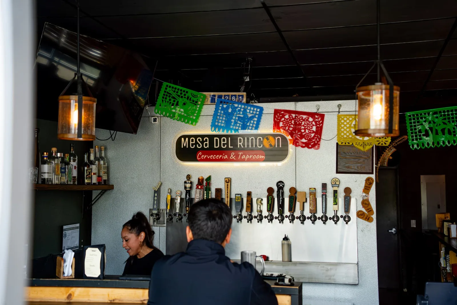 The Mesa del Rincon bar with its glowing sign, tap handles, and warm pendant lights