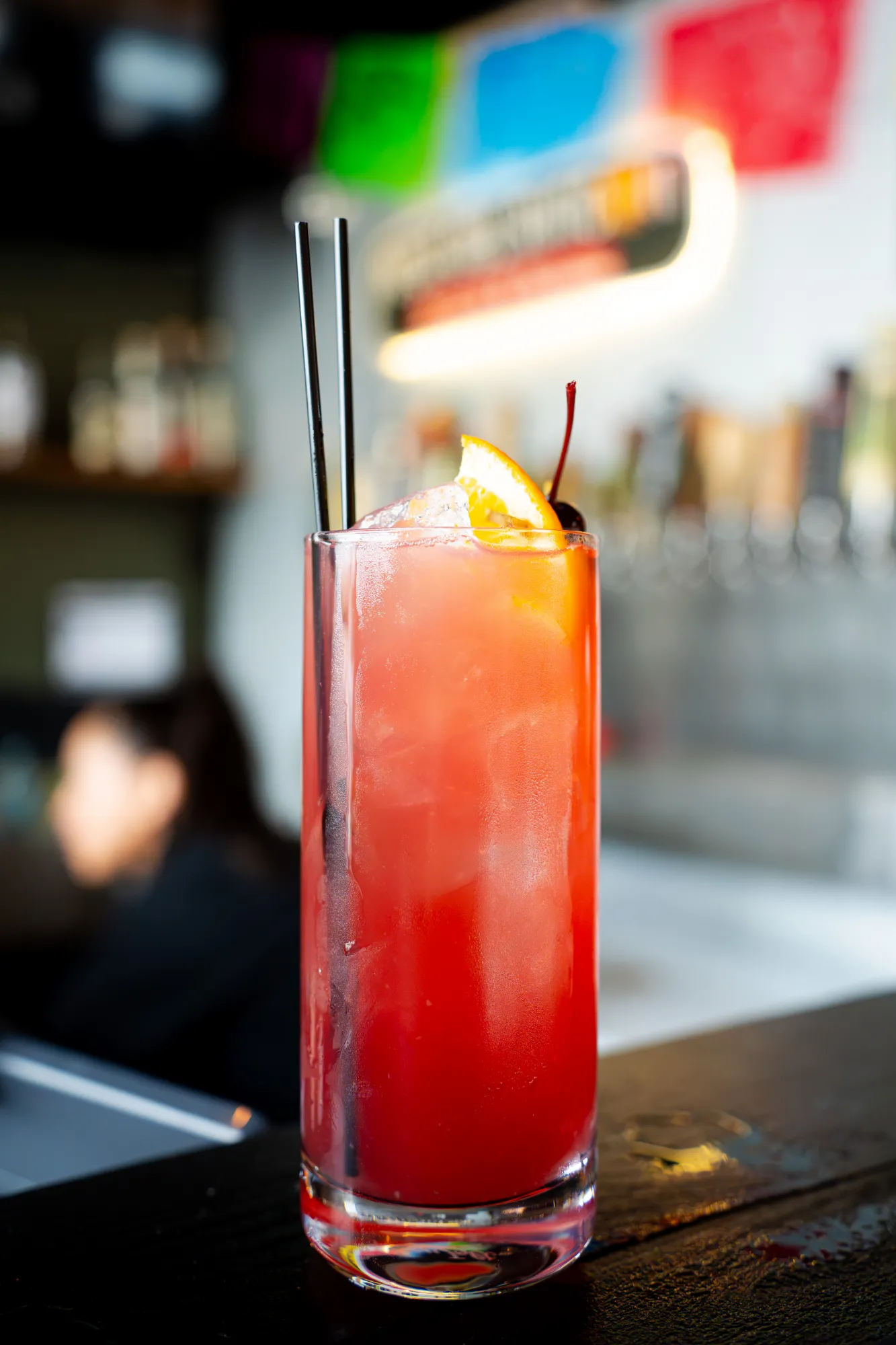 Red layered cocktail with orange and cherry garnish